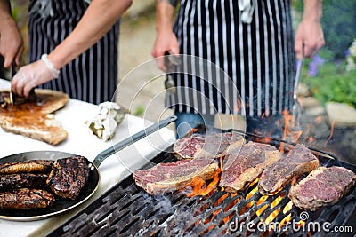 Steaks grilling on open flame and chef hands slicing steak in background Stock Photo