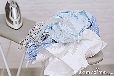 Steam iron on ironing board next to pile of cotton shirts Stock Photo