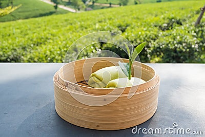 Steamed bun and green tea leaves in battered bamboo on table with tea plantation background Stock Photo