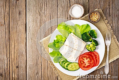 Steamed cod fish. Paleo, keto, fodmap healthy diet with vegetables on white plate on white table, side view. Stock Photo