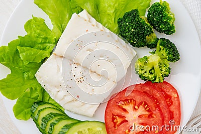 Steamed cod fish. Paleo, keto, fodmap healthy diet with vegetables on white plate on white table, top view. Stock Photo