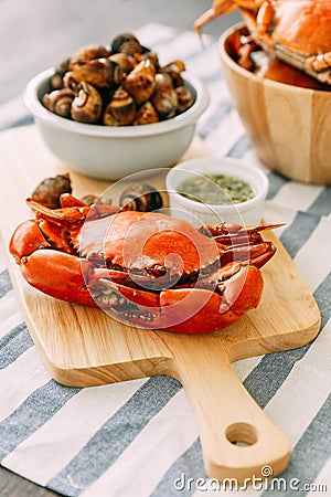 Steamed Giant Mud Crab on wooden chopping board served with Thai spicy seafood sauce and Grilled Laevistrombus Canarium in shell. Stock Photo