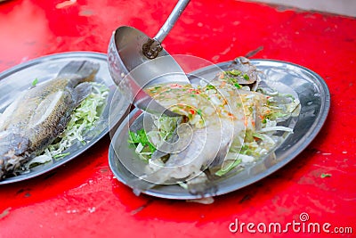 Steamed sea bass fish with lemon, Thai famous local food served on fish shape plate. Stock Photo