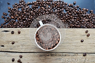 Steaming cup of coffee full of coffee beans in vintage wooden table with scattered beans around Stock Photo