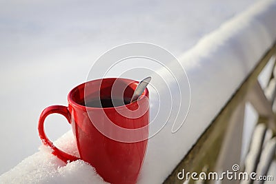 Steaming Cup of Hot Coffee or Tea standing on the Outdoor Table in Snowy Winter Morning. Cozy Festive Red Mug with a Stock Photo