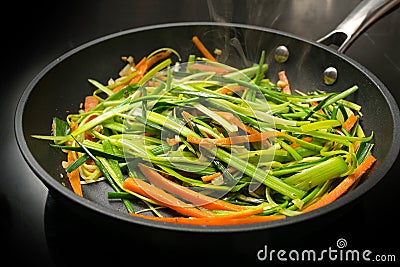 Steaming vegetable noodles from fresh carrot julienne and green leek strips in a black frying pan, cooking a healthy vegetarian Stock Photo