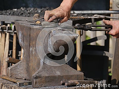 Steel anvil, on top of which lies a hot workpiece which is held by a pair of pliers. The blacksmith holds the pliers with one hand Stock Photo