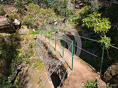 A steel cable safety fence protects tourists and hikers from a steep drop on a lavada walking trail near Monte in Funchal, Madeira Stock Photo