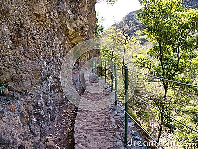 A steel cable safety fence protects tourists and hikers from a steep drop on a lavada walking trail near Monte in Madeira Stock Photo