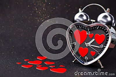 Steel Clock alarm in the form of a heart with red hearts inside and on the table on a black glitter shiny background. Happy Stock Photo