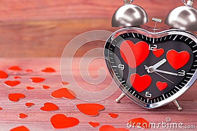 Steel clock alarm in the form of a heart, with a red hearts on a pink wooden background. Valentine`s Day Stock Photo