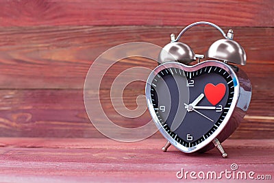 Steel clock alarm in the form of a heart, with a red heart on a pink wooden background. Valentine`s Day Stock Photo