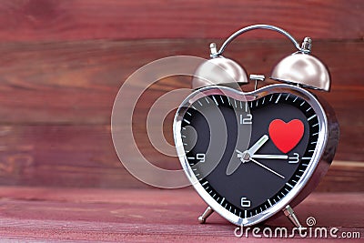 Steel clock alarm in the form of a heart, with a red heart on a pink wooden background. Valentine`s Day Stock Photo