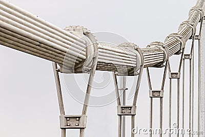 Steel thick twisted suspension bridge cable with a number of metal loops against the white sky background going into the distance Stock Photo