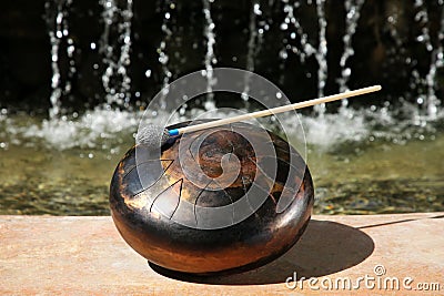 Steel tongue drum with mallet near waterfall outdoors on sunny day. Percussion musical instrument Stock Photo