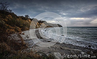 Steep coast with beach, stones and waves under a dark cloudy sky at the Baltic Sea in Mecklenburg-Western Pomerania, Germany, copy Stock Photo