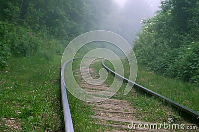 Steep turn of railways in the green forest with a misty obscure view ahead Stock Photo