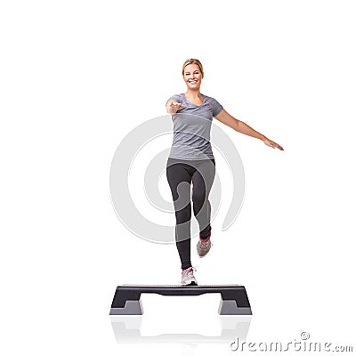 Stepping towards her fitness goals. A smiling young woman doing aerobics on an aerobics step against a white background. Stock Photo