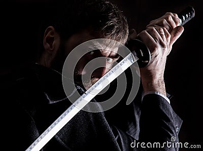 Stern angry businessman in a wool coat with sword in dark background Stock Photo