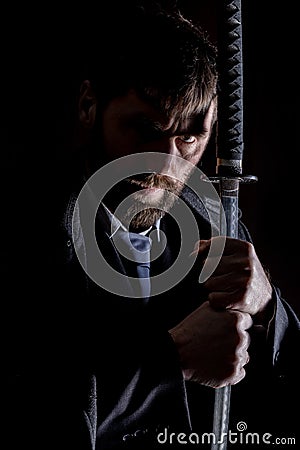 Stern angry businessman in a wool coat with sword in dark background Stock Photo