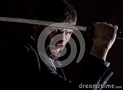 Stern angry businessman in a wool coat with sword in dark background Stock Photo