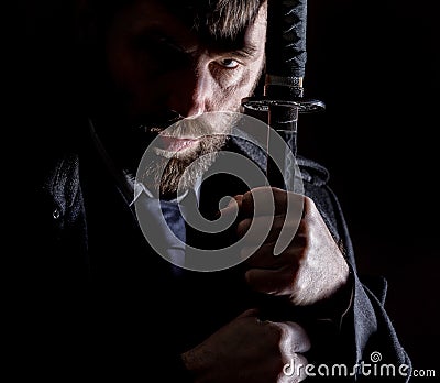 Stern angry businessman in a wool coat with sword in dark background Stock Photo