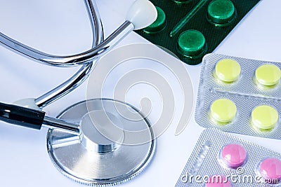 Stethoscope chestpiece is located on white background next to pills in blister pack in red, yellow and green colors in form of tra Stock Photo