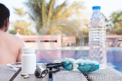 Stethoscope , drug ,swimming goggles , water and the man sitting beside the pool.Exercise and health treatment concept Stock Photo