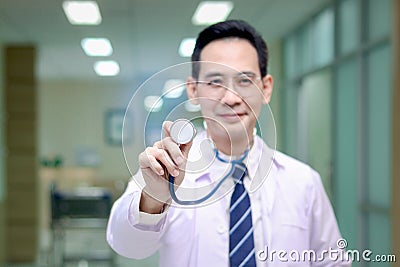 Stethoscope in hand of friendly smiling senior Asian male doctor in white workwear standing in corridor of medical clinic, happy Stock Photo