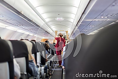 Stewardess in red uniform giving safety instructions on commercial passengers airplane. Editorial Stock Photo