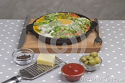 Stewed eggs and vegetables in a pan, shakshouka for breakfast. Cheese, grater, olives, peppers Stock Photo