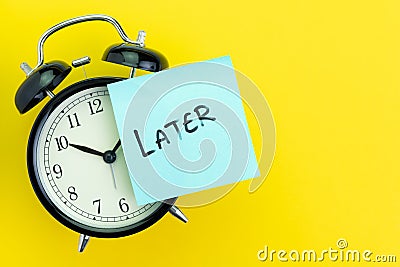 Sticky post with handwriting the word Later stick on alarm clock on solid yellow background with copy space using as Stock Photo