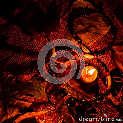 Autumn night scene of a candle dried leaves and a seed bead necklace Stock Photo