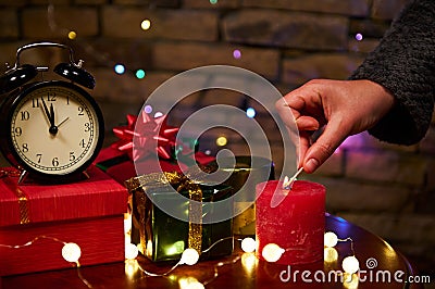 Black alarm clock with midnight on dial and woman's hand lights candle with matches. Merry Christmas Stock Photo