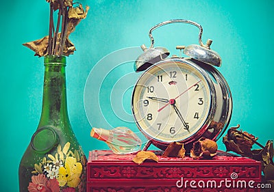 Still life with broken alarm clock, old glass vase with dead rose, perfume, vintage box Stock Photo