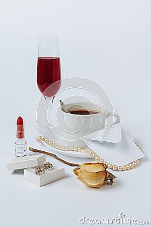 A still life with a ceramic cup of coffee, a faded rose, a coral necklace, a lipstick, a box with the silver earrings, a Stock Photo