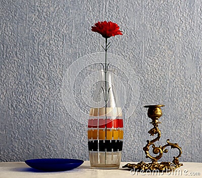 Still life. Colored glass bottle and artificial red flower. Stock Photo