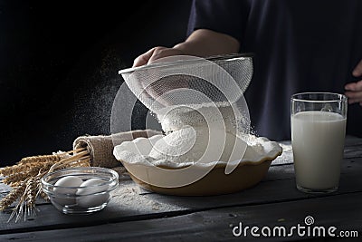 Still life on dark wooden surface. Flour sifting process. Dough ingredients next to bowl with flour. Stock Photo