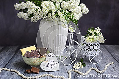 Still life details, bowl with chocolate and decorative bike with flowers, white beads and a wooden heart on a gray rustic Stock Photo