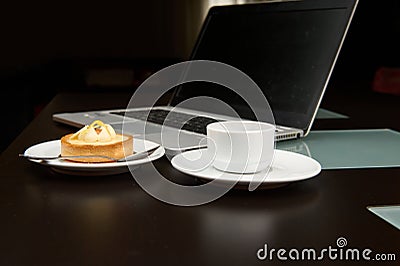 A sweet delicious tartlet with lemon custard, a cup of freshly brewed espresso coffee over the background of a laptop Stock Photo