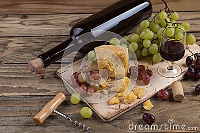 Still life from food and wine. The piece of hard cheese lies on a chopping board. Clusters of red and green mature grapes, a dark Stock Photo