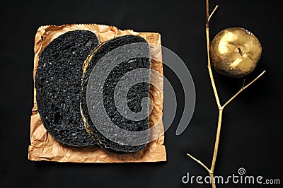 Still life image with charcoal bread on a black background with golden apple Stock Photo