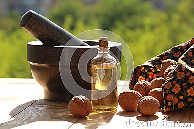 Still life of a mortar, scattered nuts and a bottle of oil against blurred green background Stock Photo