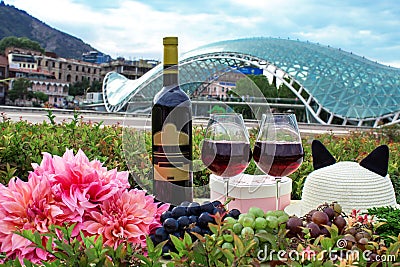 Still life on the nature of grapes, wine, hats and flowers on the background of the glass bridge of the world in Tbilisi, Georgia. Editorial Stock Photo