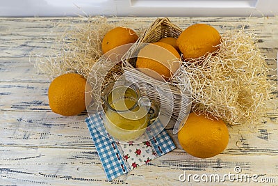 Still life with oranges, basket and glass jug with juice on old bright wooden background Stock Photo