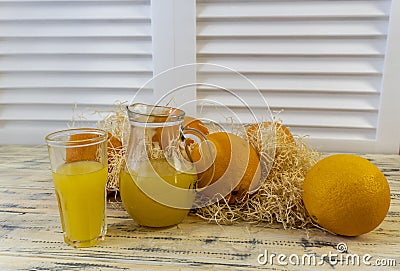 Still life with oranges, basket and glass jug with juice on old bright wooden background Stock Photo