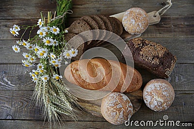 Still life of rye bread with sesame and buns and a loaf of white bread with ears and flowers on a rustic wooden background, top vi Stock Photo
