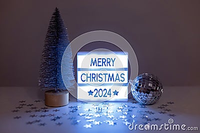 Still life with a silver Christmas tree, a disco ball and a lightbox with the inscription Merry Christmas 2024 Stock Photo