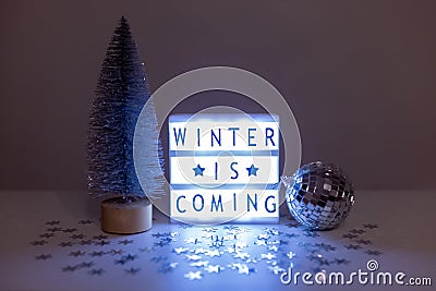 Still life with a silver Christmas tree, a disco ball and a lightbox with the inscription Winter is coming Stock Photo