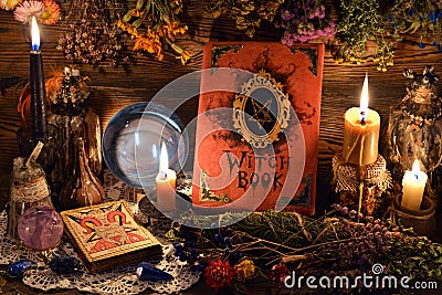 Still life with tarot cards, crystal ball, candles and witch book with hanging herbs on table Stock Photo